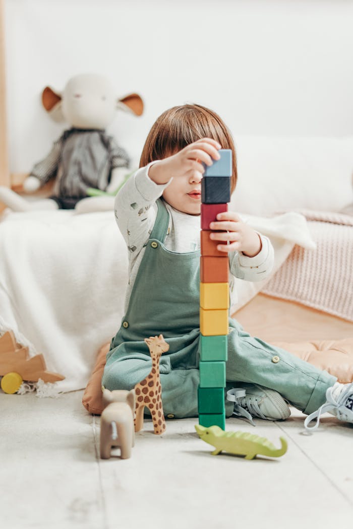 A cute child stacks colorful wooden blocks while playing indoors, surrounded by toys.